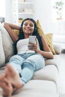 Enjoying music.  Young beautiful woman listening music and smiling while lying on the sofa at home photo