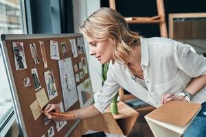 todo debe ser planeado. mujer joven atractiva escribiendo algo en la nota adhesiva mientras está de pie en el taller foto