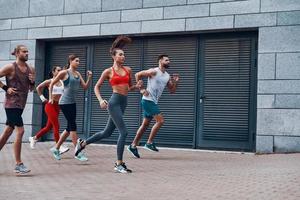 Group of young people in sports clothing jogging while exercising on the sidewalk outdoors photo