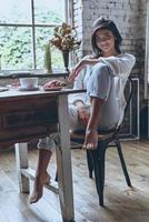 belleza despreocupada. mujer joven atractiva mirando a la cámara y sonriendo mientras desayuna en casa foto