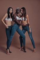 Looking perfect. Full length of three attractive young women looking at camera while standing against brown background photo