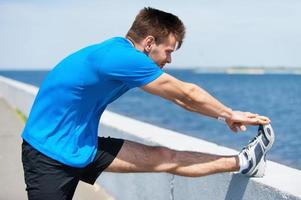 Warming up. Handsome young man doing stretching exercises while standing outdoors photo