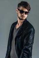 Fashion model. Confident young man in sunglasses looking away while standing against grey background photo