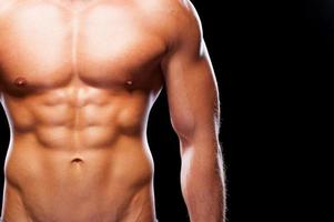 Looking ideal. Close-up of young muscular man with perfect torso standing against black background photo