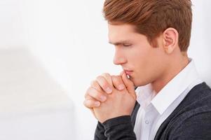 Worried about business. Side view of thoughtful young man holding hands clasped near mouth and looking down while standing isolated on white photo