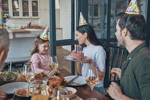 familia feliz celebrando el cumpleaños de una niña sentada en la mesa del comedor en casa foto