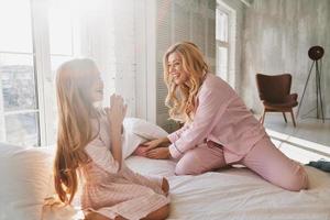 Feeling so excited. Young attractive mother taking a present to give to her cute little daughter while sitting on the bed at home photo