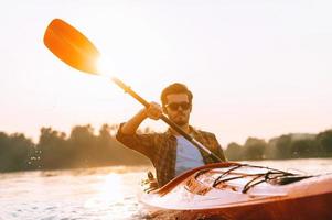 Man kayaking. Handsome young man kayaking on river with sunset in the background photo