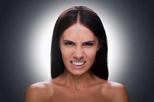 Furious beauty. Portrait of furious young shirtless woman looking at camera and grimacing while standing against grey background photo