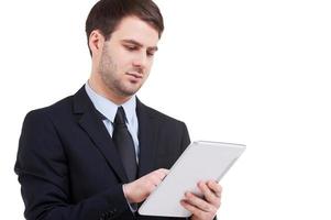 Working on digital tablet. Confident young man in formalwear working on digital tablet while standing isolated on white photo