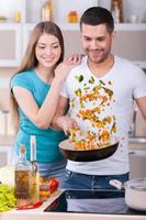 les encanta cocinar juntos. hermosa joven pareja cocinando juntos en la cocina foto