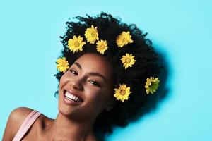 Pure beauty. Top view of attractive young African woman looking at camera and smiling while lying against blue background photo