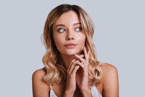 Beautiful perfection. Attractive young woman looking away and smiling while standing against grey background photo