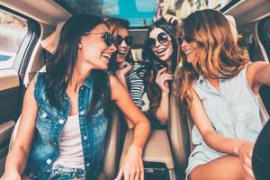 conduciendo juntos. cuatro hermosas jóvenes alegres mirándose con una sonrisa mientras están sentadas en el auto foto