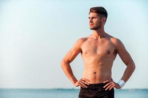 Motivation makes me moving. Confident young muscular man holding hands on hips and looking away while standing outdoors photo