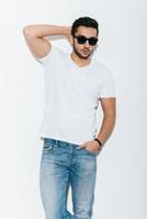 Casually handsome. Handsome young Indian man in sunglasses posing against white background photo