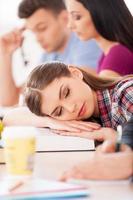 tan cansada de estudiar. hermosa estudiante durmiendo sentada en el escritorio con otros estudiantes foto