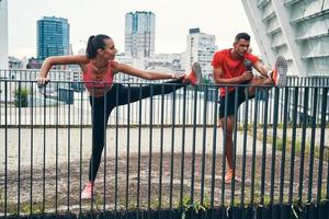 Full length of confident young couple in sports clothing warming up and stretching while practicing outdoors on the city street photo