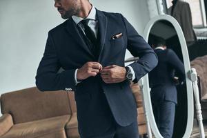 Confident in his perfect style. Close up of young man in full suit buttoning his jacket while standing indoors photo