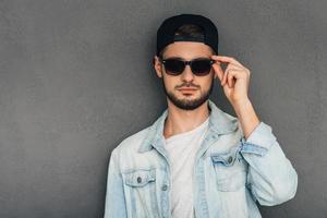 Do you like my new sunglasses Confident young man adjusting his sunglasses and looking at camera while standing against grey background photo