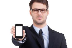 Copy space on his mobile phone. Portrait of confident young man in formalwear stretching out mobile phone and looking at camera while standing isolated on white photo