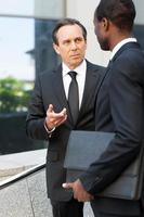 Talking about business. Two confident business men talking and gesturing while standing outdoors photo