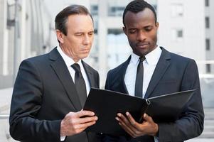 Examining documentation together. Two confident business men looking at the note pad while standing outdoors photo