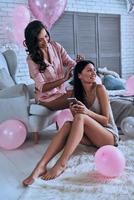 Sleepover beauty treatment. Two attractive young women in pajamas smiling while sitting in the bedroom with balloons all over the place photo