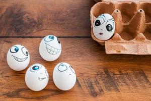 Flirty eggs. Top view of funny eggs with different emotions flirting with female egg laying in container on the wooden desk photo