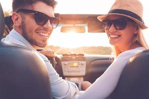 Our perfect weekend journey. Rear view of cheerful young couple looking over shoulder and smiling while sitting inside of their convertible photo