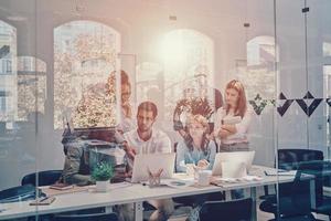 Group of young modern people in smart casual wear communicating and using modern technologies while working in the office photo