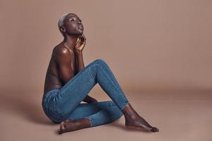 Natural and beautiful. Attractive young African woman looking away while sitting against brown background photo