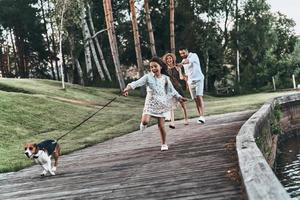 Carefree time together. Full length of cute little girl running with dog and smiling while her parents walking behind photo