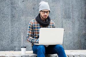 navegar por la red al aire libre. un joven apuesto que trabaja en una laptop mientras se sienta al aire libre foto