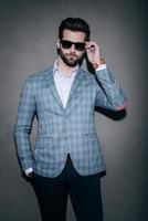 Mr. Style. Handsome young man adjusting his sunglasses and looking at camera while standing against grey background photo