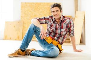 Handyman relaxing. Handsome young handyman in talking on the mobile phone and smiling while sitting on the floor photo