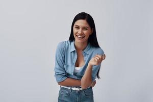 mujer joven atractiva mirando a la cámara y riendo mientras está de pie contra el fondo gris foto