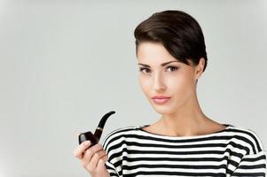 Beauty smoking pipe. Attractive young short hair woman in striped clothing holding pipe and looking at camera photo