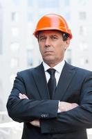 Confident contractor. Confident mature man in formalwear and hardhat keeping arms crossed and looking at camera while standing outdoors photo