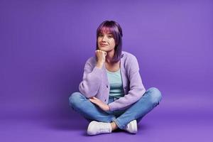 Beautiful young woman holding hand on chin while sitting against purple background photo