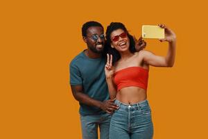 Beautiful young African couple smiling and taking selfie while standing against yellow background photo