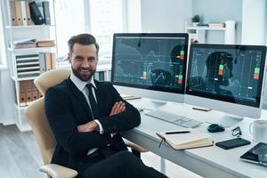 Good looking young man in formalwear smiling and looking at camera while working in the office photo