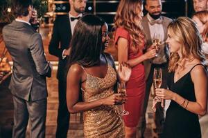 Group of beautiful young people in formalwear communicating and smiling while spending time on luxury party photo