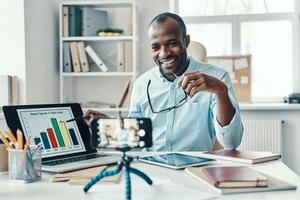 Charming young African man in shirt showing chart while making social media video photo