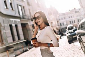 Attractive young woman talking on smart phone and looking away while walking outdoors photo