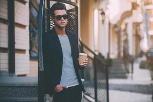 Enjoying fresh coffee. Handsome young man in smart casual wear holding coffee cup while standing on the street photo