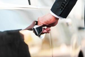 His business car. Close-up of businessman holding hand on door handle while opening his car photo