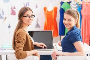 They got creative mind. Rear view of two beautiful female designers looking over shoulder and smiling while sitting at the working place photo