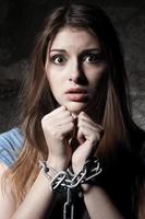 Trapped woman. Shocked young woman looking at camera while trapped in chains while standing against dark background