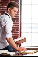 He loves studying. Handsome young man in shirt and tie writing something in note pad while sitting at his working place photo